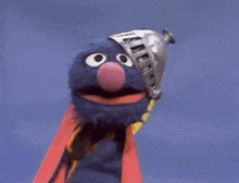 elmo from sesame street is wearing a cape and holding a book .
