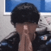 a man with his hands folded in front of his face is sitting in front of a window .