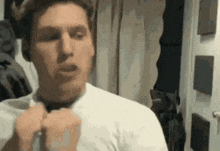 a man wearing headphones and a white shirt is looking at himself in the mirror .