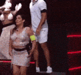 a woman in a white dress is dancing on a stage with a man standing behind her .