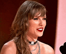 taylor swift is wearing a choker necklace and red lipstick while talking into a microphone .