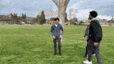 a group of young men are standing in a grassy field with a tree in the background