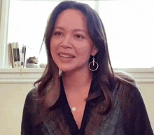 a woman wearing hoop earrings and a necklace smiles for the camera