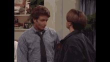a man in a plaid shirt and tie talks to another man in a black jacket