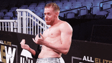 a shirtless wrestler stands in front of a wall that says all elite