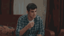 a man in a plaid shirt sits on a couch eating something