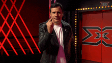 a man in a leather jacket stands in front of a red door with a x on it