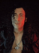 a man with long curly hair is wearing a necklace with a dragon pendant