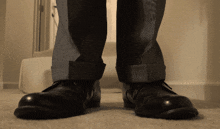a person wearing a pair of black shoes is standing on a carpeted floor