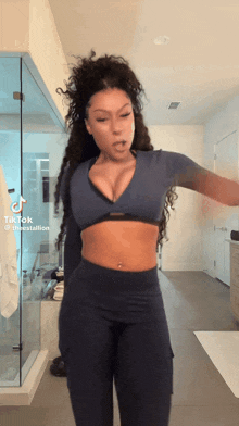 a woman is standing in a bathroom wearing a blue crop top and black pants .