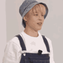 a young man wearing a denim hat and overalls is making a funny face .