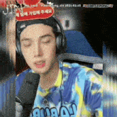 a young man wearing headphones and a tie dye shirt is talking into a microphone ..