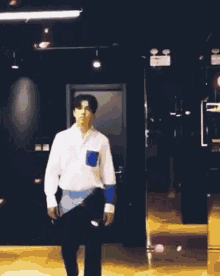 a man wearing a white shirt with a blue pocket is standing in a dark room .