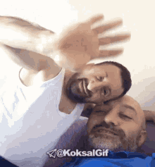 two men are laying on a couch and one of them is wearing a blue shirt and the other has a white tank top on