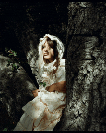 a woman in a white dress with a hood is sitting under a tree