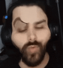 a man with a beard is wearing headphones and making a funny face with his eyes closed .