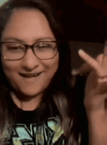 a woman wearing glasses and a black shirt is making a peace sign with her hand .