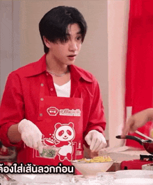 a man wearing a red apron with a panda on it prepares food