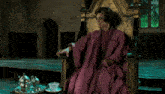a woman in a purple robe sits on a gold chair