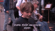 a young boy talking into a microphone while wearing a shirt that says stupid poop um you 're ugwy