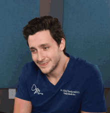 a man wearing a blue shirt that says dr. mikhail varshavski d.o. family medicine laughs with his mouth open