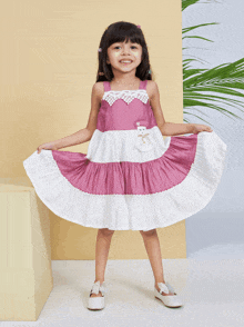 a little girl is wearing a pink and white dress and white shoes