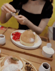 a woman is sitting at a table with a plate of pancakes and strawberries