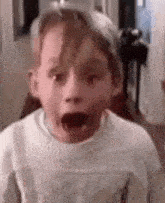 a young boy is making a surprised face while wearing a white sweater .