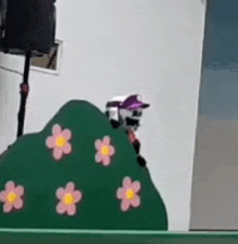 a cartoon character is standing on top of a green hill with pink flowers .