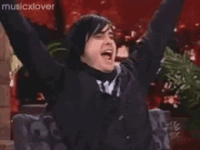 a man in a black hoodie is raising his arms in the air while dancing .