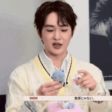 a man in a white sweater holds a stuffed animal with the word onew on the bottom