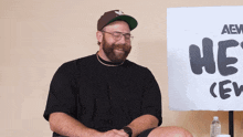 a man wearing a hat and glasses sits in front of a sign that says he 's crew