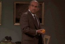 a man in a suit holds an orange in his hand