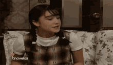 a girl with pigtails is sitting on a couch in front of a tv screen that says tnovelas