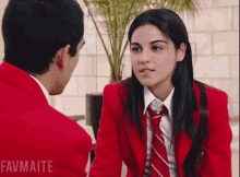 a girl in a red jacket and tie is talking to a boy in a red jacket