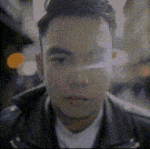 a man wearing a leather jacket and a white shirt is looking at the camera in a pixelated image .