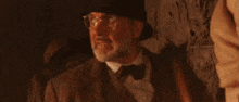 a man with a beard and glasses wearing a hat and bow tie is standing in a dark room .