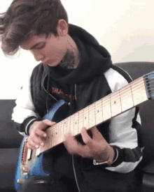 a young man in a black and white jacket is playing a blue electric guitar