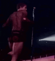 a man is singing into a microphone on a stage while wearing shorts .
