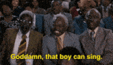 a group of men in suits and ties are sitting in a crowd and one of them is saying goddamn that boy can sing