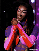 a drag queen wearing a purple and pink outfit with red gloves