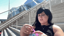 a woman sitting on a set of stairs holding a pink object in her hand