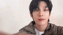 a young man wearing a plaid shirt and a white shirt is taking a selfie .
