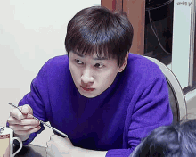 a man in a purple sweater is holding chopsticks in his hand