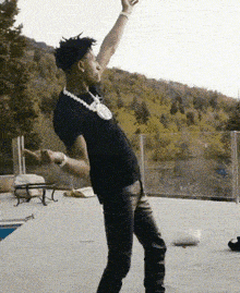 a man wearing a black shirt and a necklace is dancing on a patio .