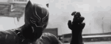 a black and white photo of a black panther in a black suit holding a gun .