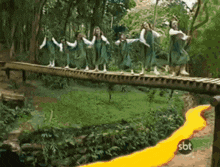 a group of girls are walking across a wooden bridge with a sbt logo on the bottom