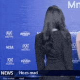 a woman standing in front of a blue wall with the words hoes mad on it