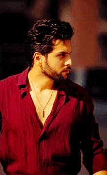 a man with a beard and a necklace is wearing a red shirt .