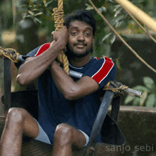 a man is sitting in a chair with the name sanjo_sebi written on the bottom